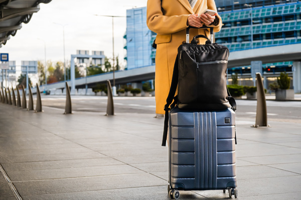 person waiting outside airport at pickup with luggage, on phone booking taxi concept