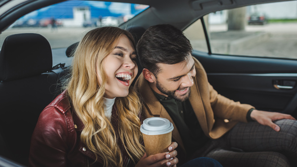 smiling, laughing young couple, back of taxi with coffee cup in hand